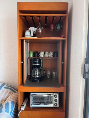 Ein Holzkabinent mit Regalen, inklusive Kaffeemaschine, Tassen und Toaster.
