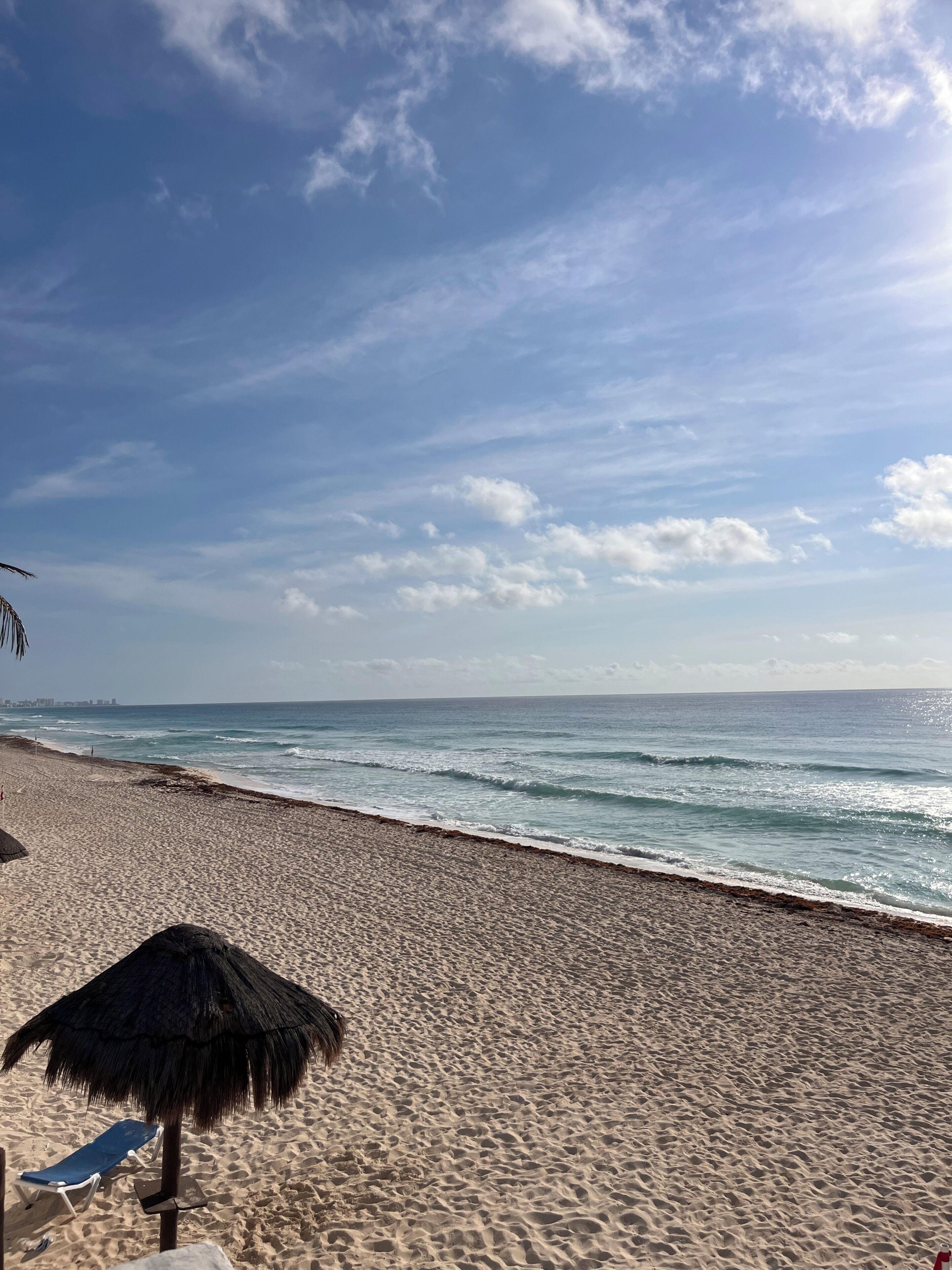 Une plage avec un parasol en chaume et une chaise longue bleue.