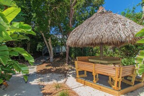 Eine Holzterrasse mit einem reetgedeckten Dach, umgeben von üppigem Grün und Bäumen.
