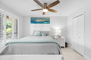 Ein Schlafzimmer mit einem Bett, einem Nachttisch, einem Wandbild und einem Deckenventilator.