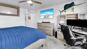 Een slaapkamer met een bed, een bureau met een computer, een stoel, een plafondventilator en een grote visdecoratie aan de muur.