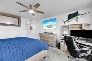 Ein Schlafzimmer mit einem Bett, einem Schreibtisch mit Computer, einem Stuhl, einem Deckenventilator und einer großen Fischdekoration an der Wand.