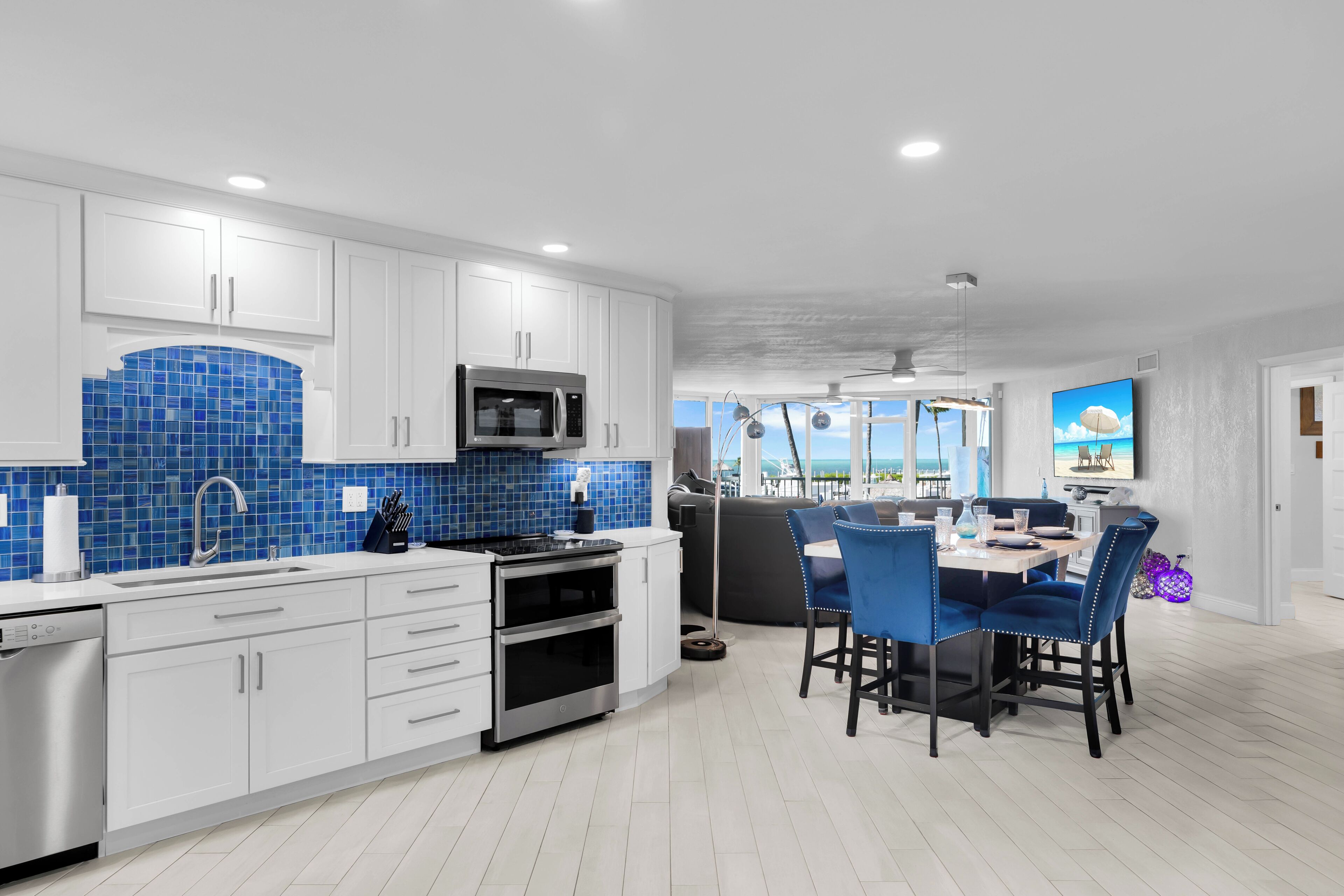 Een moderne keuken met witte kastjes, een blauwe spatwand, en een eethoek met blauwe stoelen.