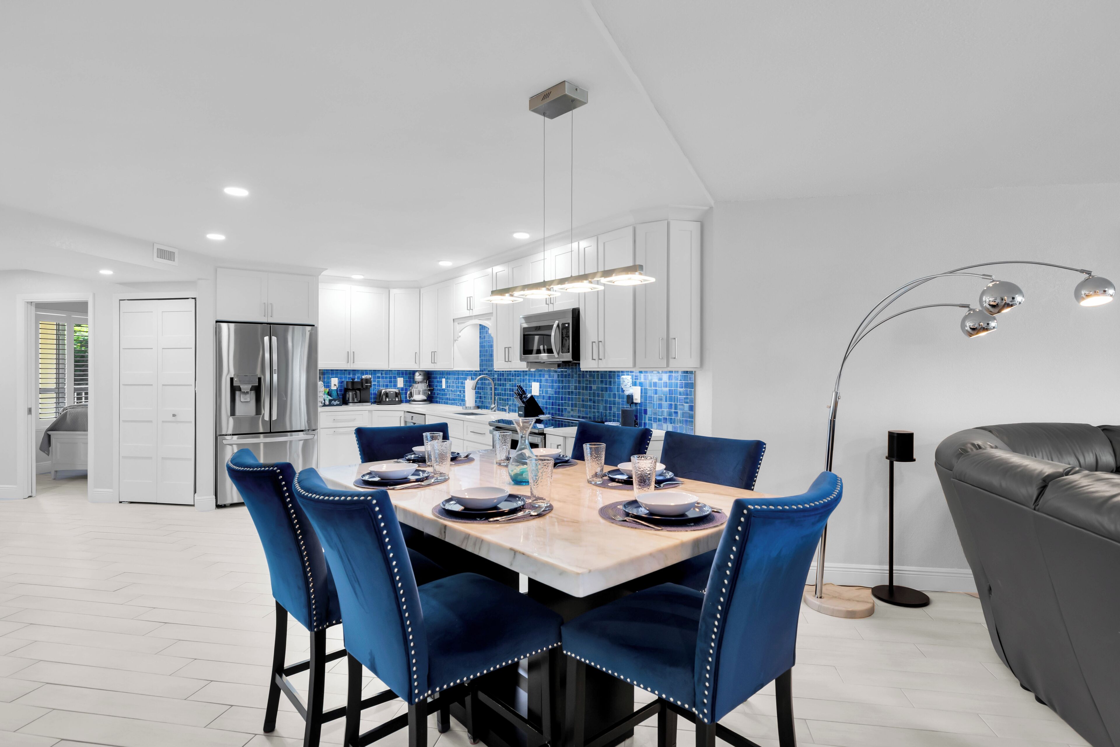 A modern kitchen with white cabinets, a stainless steel refrigerator, and a blue-tiled backsplash.