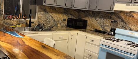 A kitchen with a wooden countertop, a gas stove, cabinets, and a microwave.