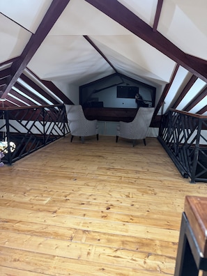 An attic room with a sloped ceiling, wooden flooring, and a large window.