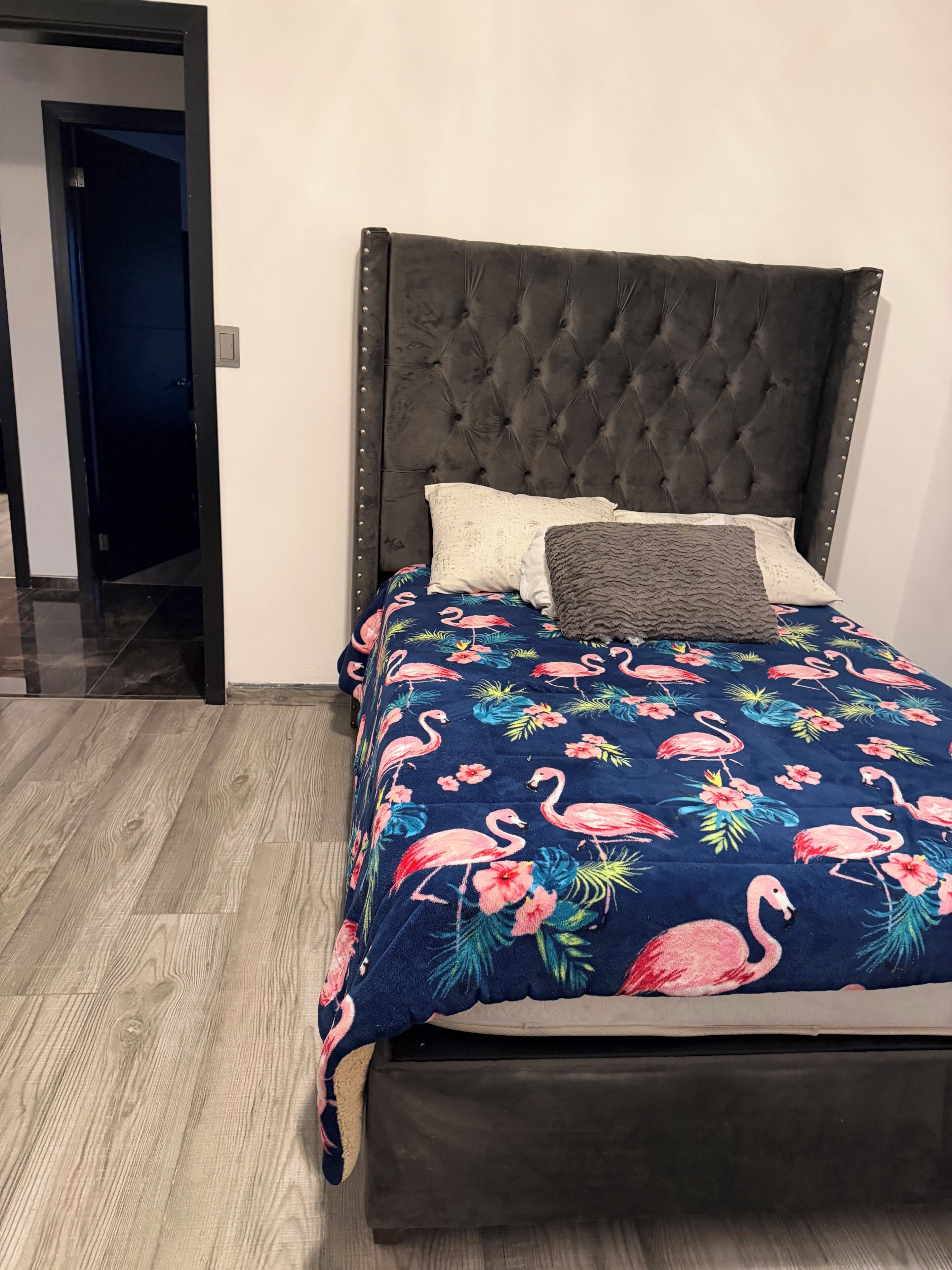 Un dormitorio con cabecera capitonada, cama con colcha estampada y suelo de madera.