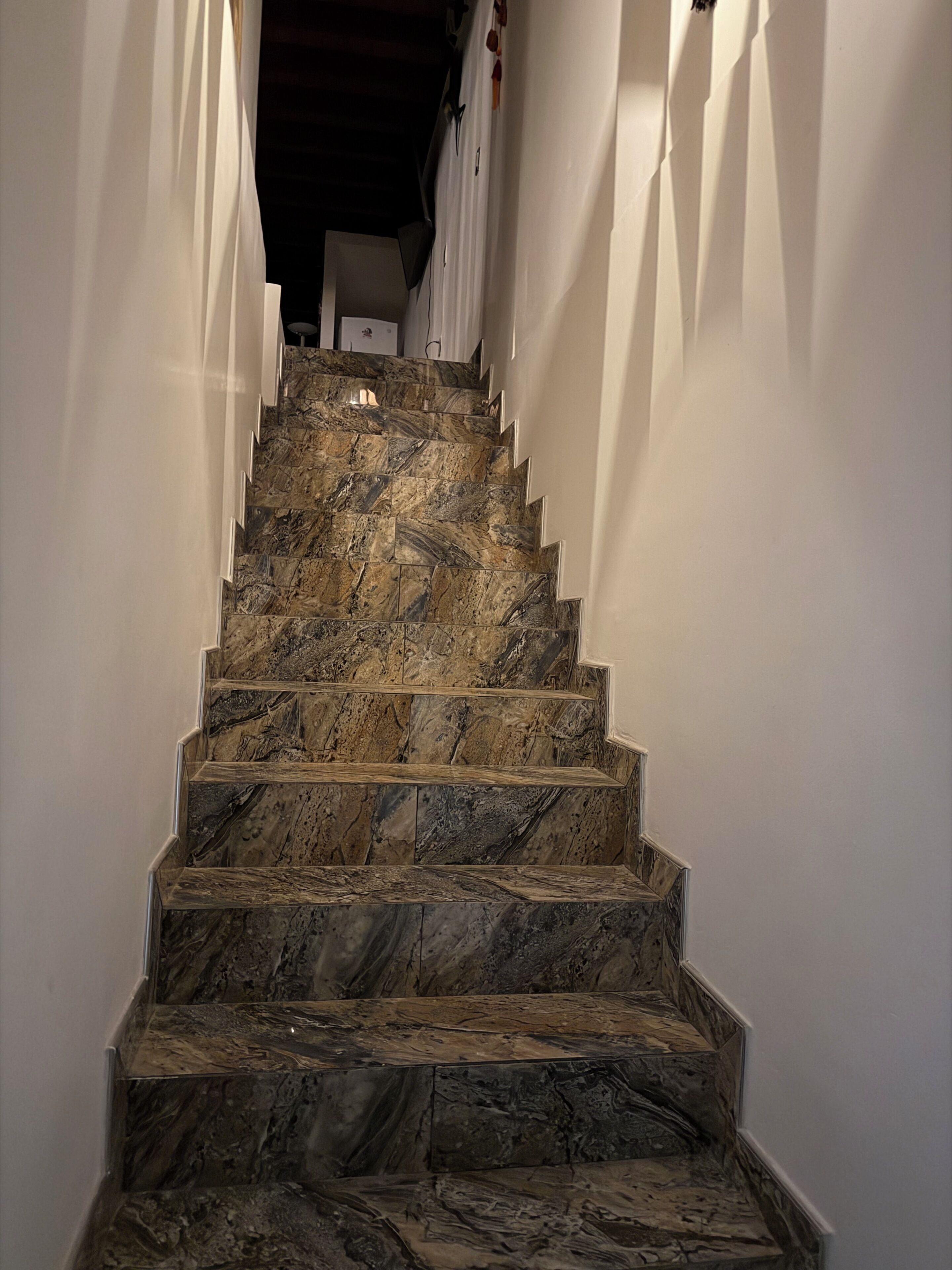 A staircase with marble steps leading upwards, flanked by white walls, and a light fixture at the top.
