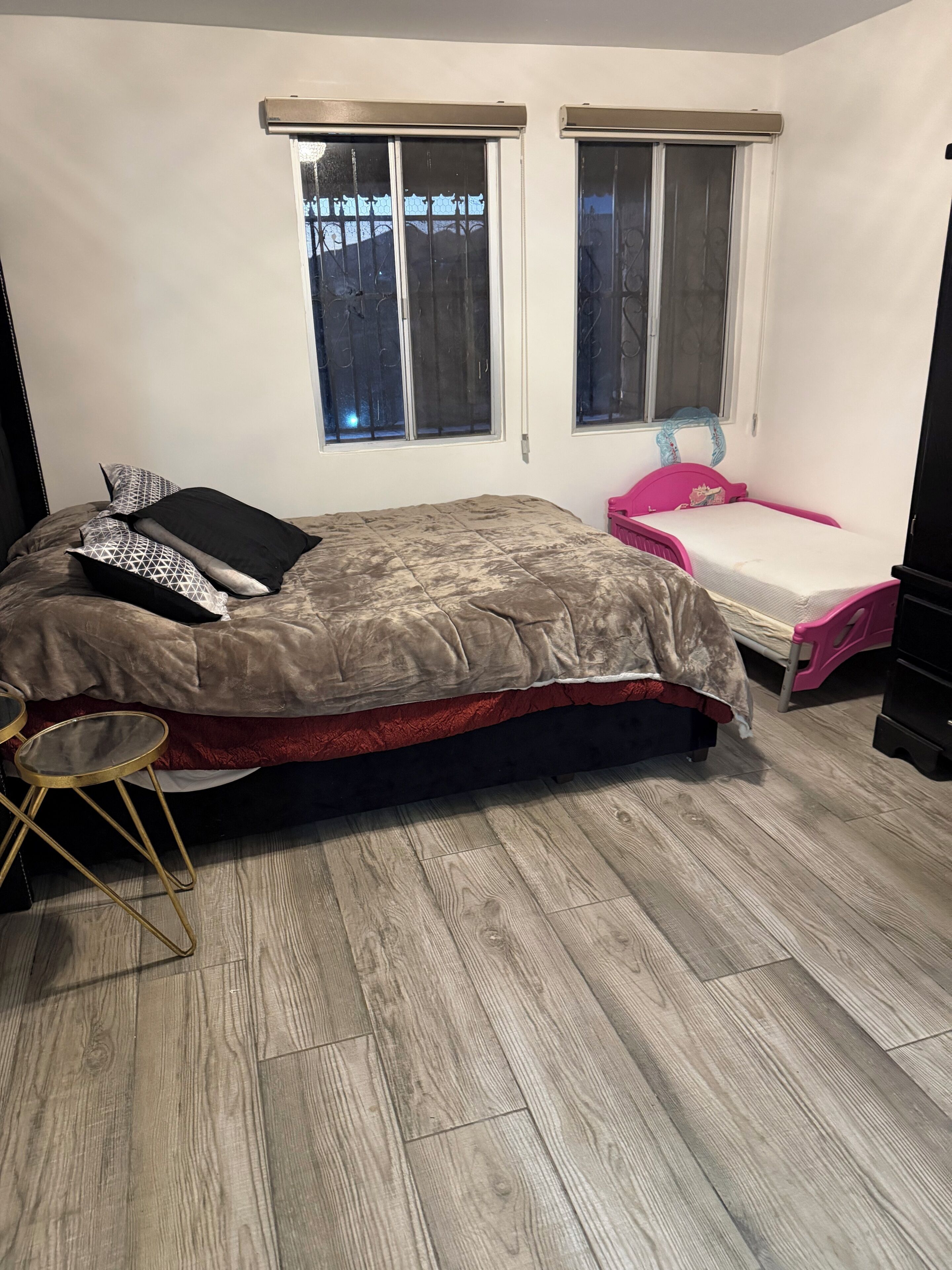 Een slaapkamer met een bed, een klein tafeltje, een roze stoel en twee ramen.