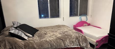 Ein Schlafzimmer mit einem Bett, einem kleinen Tisch, einem rosa Sessel und zwei Fenstern.