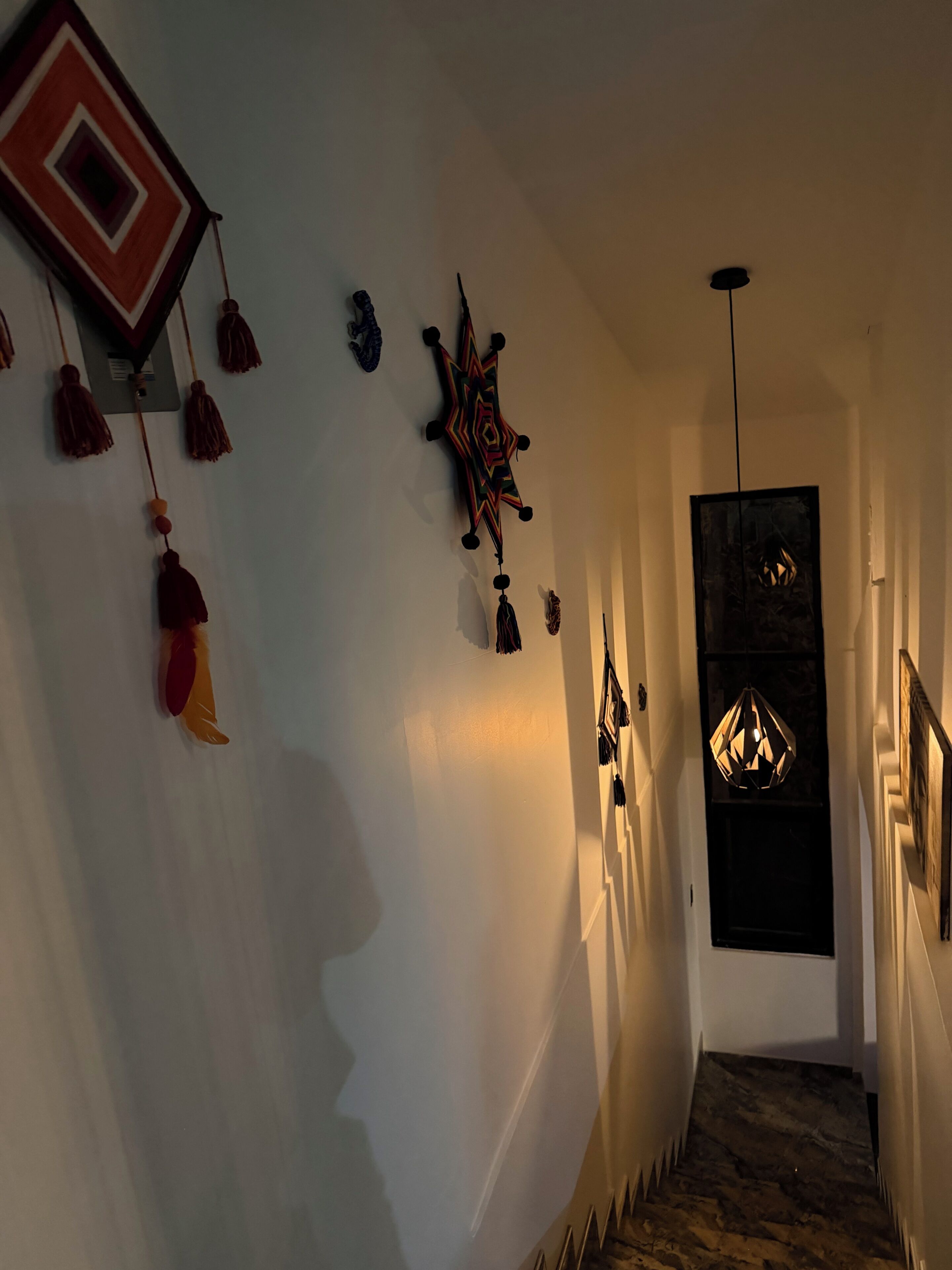 A hallway with a staircase, a geometric wall decoration, and a hanging light fixture.