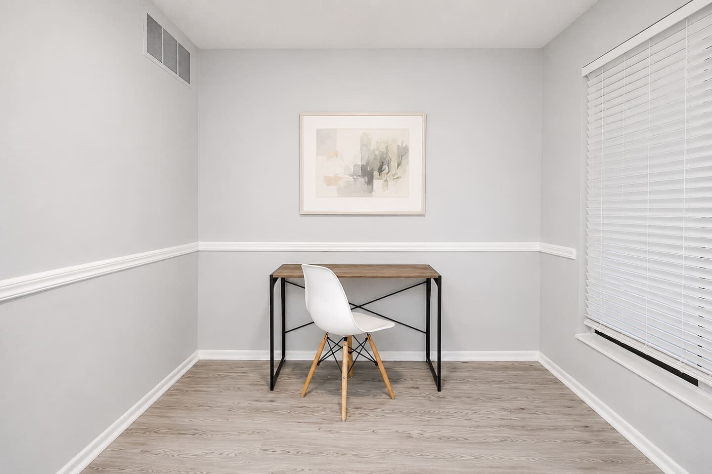 A corner room with a white chair, a wooden table, and a framed picture on the wall.