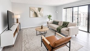 A modern living room with a flat-screen TV, a sofa, a coffee table, and a leather chair.