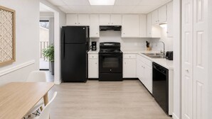 A compact kitchen with white cabinets, a black refrigerator, a stove, and a dishwasher.