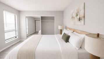A hotel room with a bed, bedside lamps, a painting on the wall, and a view of the hallway.
