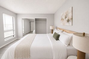 A hotel room with a bed, bedside lamps, a painting on the wall, and a view of the hallway. - Sleepover | Comfortable 1BD/1BA + Gym - Wichita (Wichita)