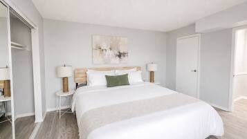A bedroom with a large bed, two bedside tables with lamps, a wooden headboard, a wall-mounted abstract painting, and a wardrobe.
