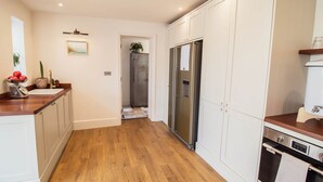 Une cuisine avec un plancher en bois, des armoires blanches, un réfrigérateur en acier inoxydable et un comptoir en bois.