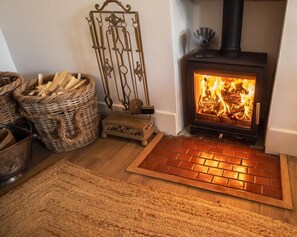 A wood-burning stove with a brick hearth, wicker baskets, and a metal decorative piece. - Vereeniging Holiday Home (Seaford)