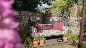 Un parterre de fleurs agrémenté d’un banc en bois, entouré de plantes en pot et d’un mur de pierres.