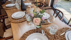 Une table à manger dressée avec des assiettes, des couverts, des verres et un centre de table composé de fleurs.