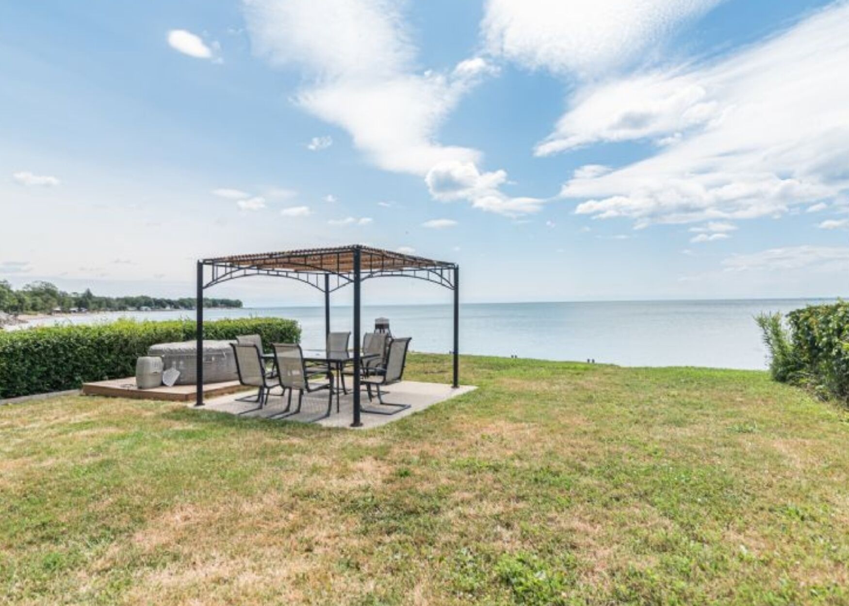 A gazebo with outdoor seating, a grill, and a view of the water.
