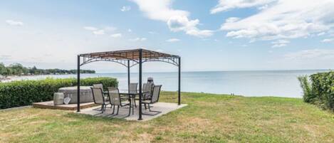 A gazebo with outdoor seating, a grill, and a view of the water.