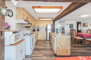 A kitchen with wooden cabinets, a stove, microwave, and refrigerator. There is a dining area with a table and chairs.