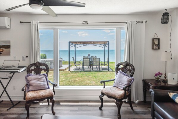 A room with a view of the sea, two upholstered chairs, a desk with a keyboard, and a ceiling fan.