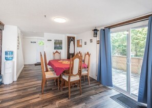 Comedor con una mesa para cuatro, sillas de madera, dispensador de agua y vista a una terraza exterior a través de un vidrio.