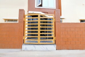 A gated entrance with a marble base, a yellow metal gate, and a brick wall. - Collection O Kolkata International (Barakpur)