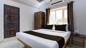 A hotel room with a bed, a wardrobe, a nightstand, an air conditioning unit, and a window with curtains.