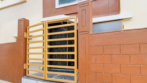 A yellow metal gate with horizontal bars, attached to a building with a brick wall and a window above it.