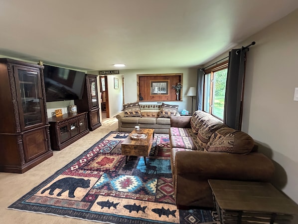 A living room with a large TV, a sofa, a coffee table, and a patterned rug.
