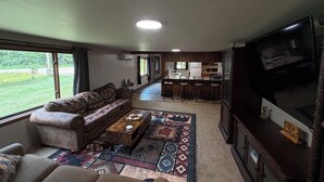 En stue med sofa, sofabord og fjernsyn. Der er et køkkenområde med bar og spisebord.