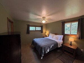 Ein Schlafzimmer mit einem Bett, einem Nachttisch, einem Deckenventilator und einem Fenster mit Vorhängen.