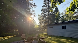 En baghave med træterrasse, Adirondack-stole og et lille skur.
