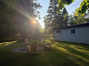 Ein Garten mit einer Holzterrasse, Adirondack-Stühlen und einem kleinen Schuppen.