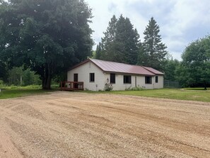 A single-story building with a metal roof, a wooden deck, and a gravel driveway.