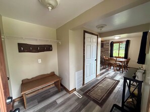 A hallway with a bench, a door, a coat rack, a dining area with a table and chairs, and a rug.