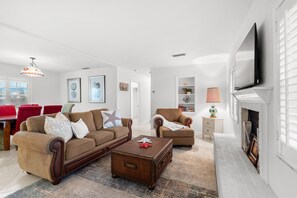 Ein Wohnzimmer mit Sofa, Sessel, Couchtisch, Kamin und Fernseher.