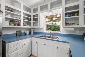 A modern kitchen with white cabinetry, a blue countertop, and a window with a view of greenery. - Melbourne Beach Escape: Private Pool & Pool Spa, Big Backyard, Steps to Beach (Melbourne Beach)