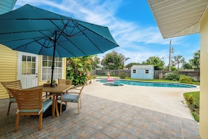 A patio with a table and chairs, a swimming pool, and a fenced backyard. - Melbourne Beach Escape: Private Pool & Pool Spa, Big Backyard, Steps to Beach (Melbourne Beach)