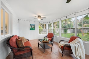 A sunroom with wicker furniture, a ceiling fan, and large windows overlooking a garden. - Melbourne Beach Escape: Private Pool & Pool Spa, Big Backyard, Steps to Beach (Melbourne Beach)