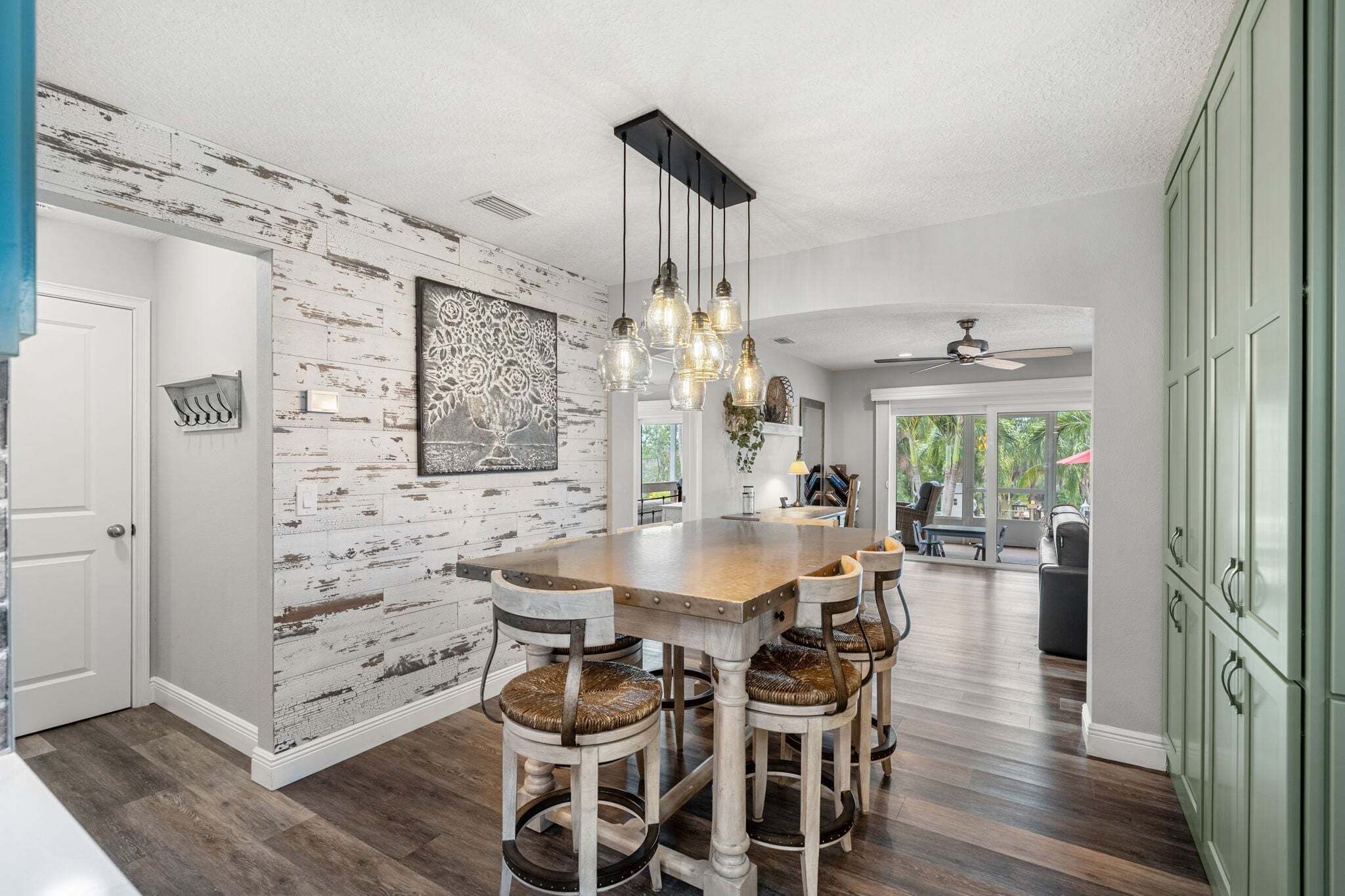 A kitchen with a rustic wooden wall, a central island with stools, and a ceiling fan.