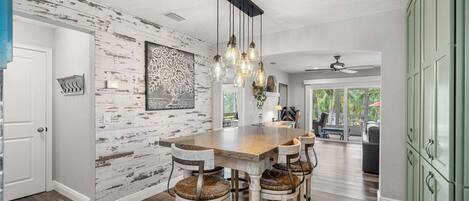 A kitchen with a rustic wooden wall, a central island with stools, and a ceiling fan.