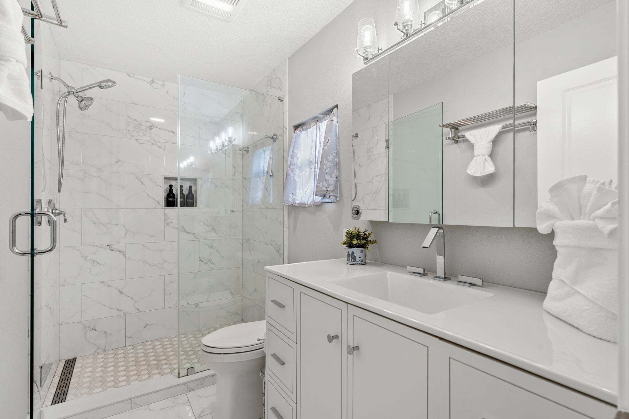 Een moderne badkamer met een glazen douchecabine, toilet, wastafel met spiegel en een handdoekhouder.