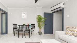 Uma sala de estar moderna com área de jantar, um sofá, uma mesa de centro, uma planta em vaso e um ar condicionado.