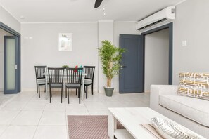 A modern living room with a dining area, a sofa, a coffee table, a potted plant, and an air conditioning unit. - Modern 1 Bedr Apartment · Stylish Aruba Stay (Noord)