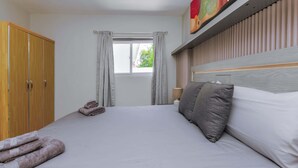 Quarto de hotel com cama, guarda-roupa, janela com cortinas e um quadro na parede.